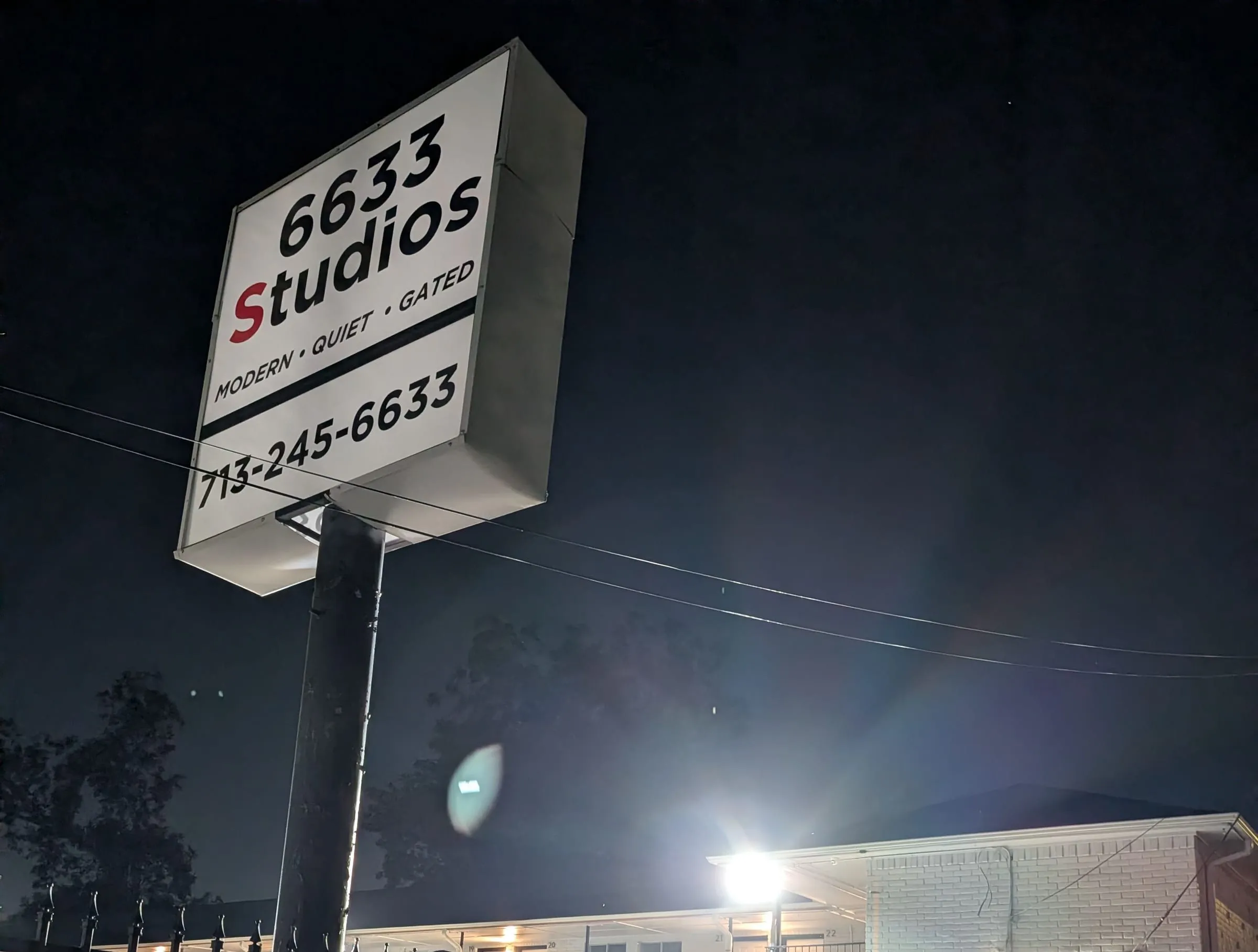 The lit 6633 Studios sign above the gated lot at night